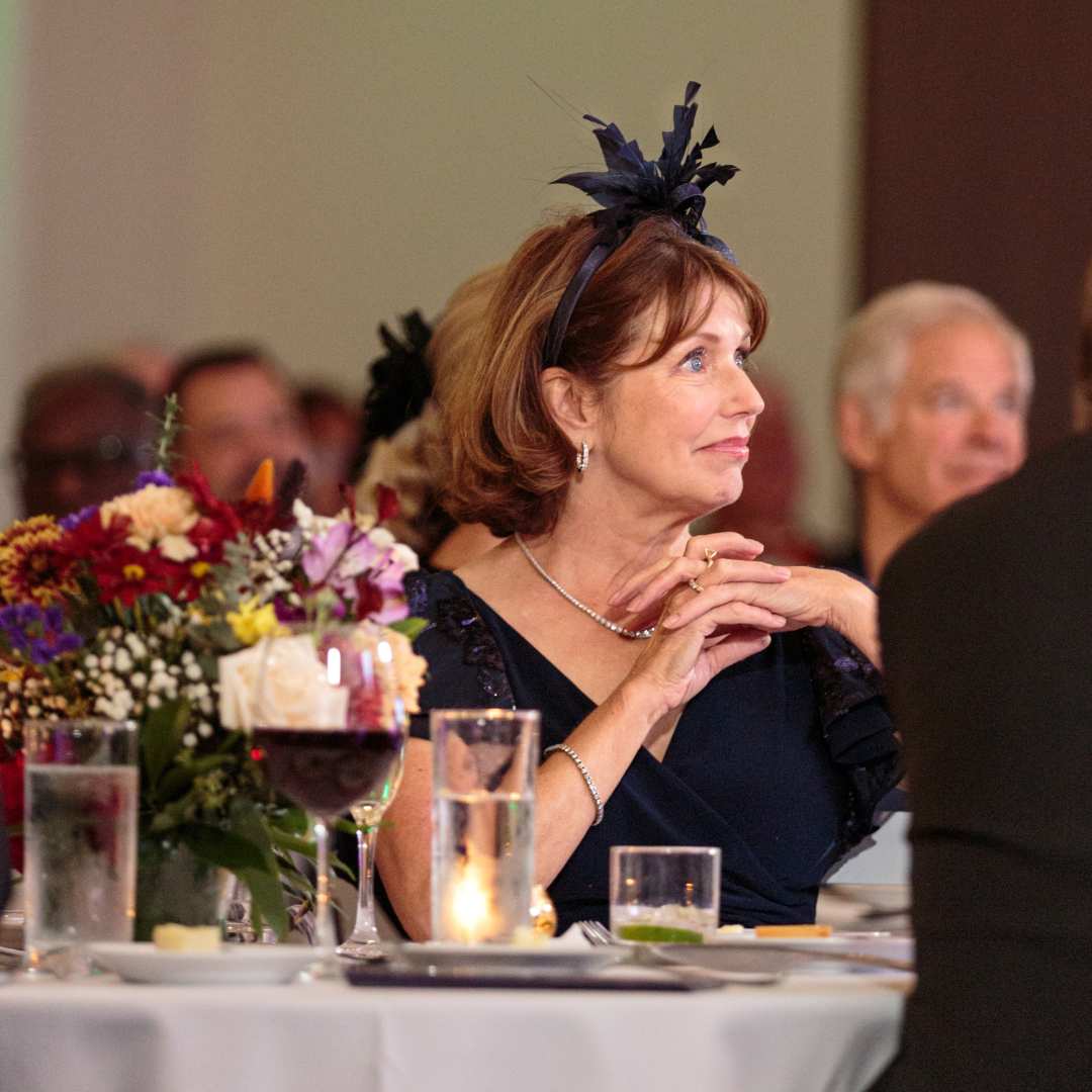 Woman wearing fascinator sitting at table with flowers